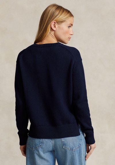 Tumši zils adīts džemperis ar ribotām aprocēm un apakšmalu, ar apaļu kakla izgriezumu un raglāna piedurknēm. Gluda tekstūra un brīvs piegriezums.