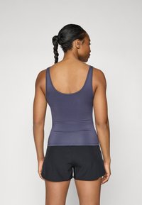 Marineblå tettsittende tank top med brede stropper og scoop bak, kombinert med svarte treningsshorts. Glatt tekstur; minimal detaljering.