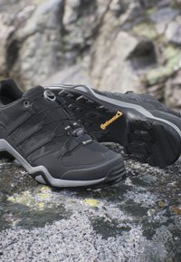 Zapatillas deportivas negras con un acabado texturizado, que cuentan con un sistema de lazada rápida y una suela de goma gris con surcos profundos para tracción.