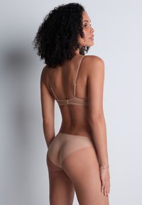 Ensemble de lingerie nude comprenant un soutien-gorge à dos transparent avec des bretelles réglables et une culotte lisse assortie. Matériau doux et flexible avec un design sans coutures.