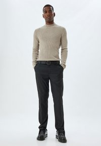 Beige geribbelde trui gecombineerd met zwarte broek en zwarte schoenen; zachte textuur, nauwsluitend ontwerp en een ronde hals.