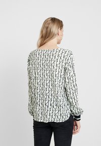 Blouse à manches longues en vert clair avec un motif floral noir. Texture douce, coupe décontractée et poignets contrastés.