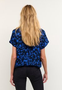 Bluse med blå blomsterprint, korte ærmer og afslappet pasform, lavet af letvægtsstof, parret med tætsiddende sorte jeans.