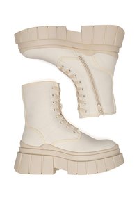 Botines tobilleros de lona beige con suela gruesa estriada, con cierre de cordones en la parte frontal y cremallera lateral para facilitar el uso.