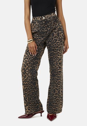 Femme portant un pantalon large à taille haute imprimé léopard, un haut noir, un bracelet doré et des escarpins bordeaux à talon kitten pointu.