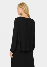 Blusa nera a maniche lunghe plissettata con scollatura rotonda e polsini arricciati, caratterizzata da una silhouette fluida e una texture morbida.