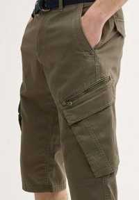 Khaki cargo shorts lavet af tekstureret stof. Har flere lommer, herunder en lynlåslomme på siden. Design med bælte i taljen.