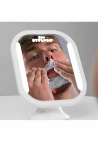 Fyrkantig spegel med en vit ram, upplysta kanter, som reflekterar en person som applicerar rakkräm på sitt ansikte med båda händerna.