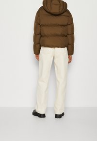 Brun puffjacka med huva, med quiltade sektioner och elastiska manschetter. Matchas med off-white vida byxor och svarta ankelboots.