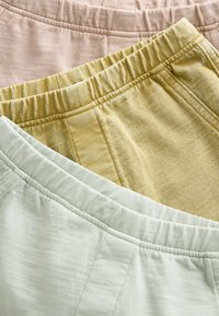 Drie paar elastische tailleband broeken van zachte stof: lichtroze, gedempt geel en bleekgroen, met een getextureerd, casual ontwerp.