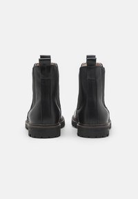 Botas de tobillo de cuero negro con acabado suave, paneles laterales elásticos y tiradores. Suelas de goma gruesa con un patrón de relieve.