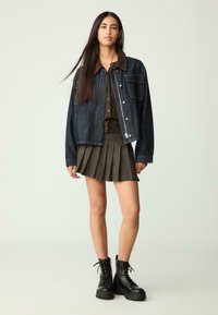 Denim takki ruskealla corduroy-kauluksella, tummansininen väri, yhdistettynä poimutettuun oliivinvihreään hameeseen ja mustiin vaelluskengiin.