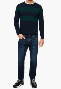 Námořnický svetr s zelenými horizontálními pruhy, kulatý výstřih, žebrované manžety. Kombinováno s tmavě modrými džíny a černými teniskami s bílými detaily.