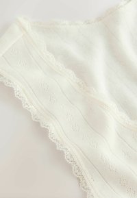 Off-white fabric with a textured pattern and scalloped lace trim. The fabric features subtle horizontal lines and raised floral motifs.