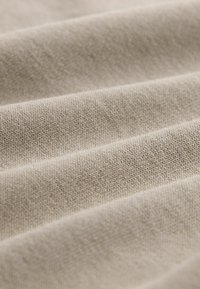 Helle beige Stoff mit strukturiertem Gewebe, das sanfte Falten aufweist, die Tiefe erzeugen. Glatte Oberfläche mit subtilen Tonvariationen.