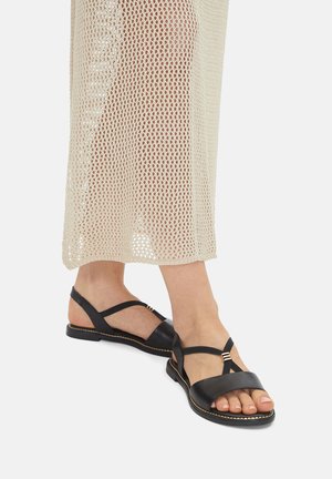 Czarne skórzane sandały z paskami krzyżującymi się na stopie, ozdobione złotymi akcentami. Płaska podeszwa i otwarty nosek.