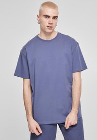 Tricou din bumbac de culoare purpuriu, cu mâneci scurte, guler rotund și croială lejeră. Materialul pare neted, fără modele sau accente vizibile.