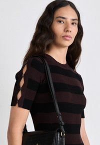 Top in maglia con righe orizzontali nere e bordeaux, maniche corte con dettagli di bottoni. La modella porta una borsa a tracolla nera con texture.