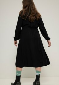Vestido negro de longitud media con mangas largas, cintura ceñida y textura suave. Estilizado con calcetines verdes y blancos y botas de tobillo con tachuelas.