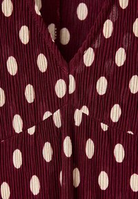 Gros plan d’un tissu bordeaux à pois blancs avec de subtils plis verticaux formant une couture en forme de V.