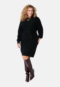 Zwarte gebreide jurk met een ceintuur in de taille, lange mouwen en geribbelde manchetten, gecombineerd met bordeaux hoge hakken met een krokodillenpatroon.