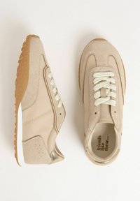 Sneaker beige con lacci bianchi e suola testurizzata, che mostrano un mix di suede e tessuto, con la frase "amici come questi" all'interno.