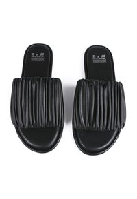 Chanclas negras con una correa de cuero plisada, suela plana y textura suave. Logo impresa en la plantilla. Diseño y color minimalistas.