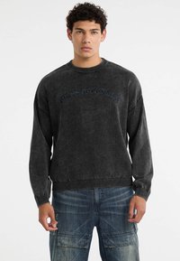 Donkergrijze sweatshirt met ribbels bij de halslijn en mouwen. Bevat het "GUESS ORIGINALS" logo in het blauw, casual oversized ontwerp met een gestructureerd oppervlak.