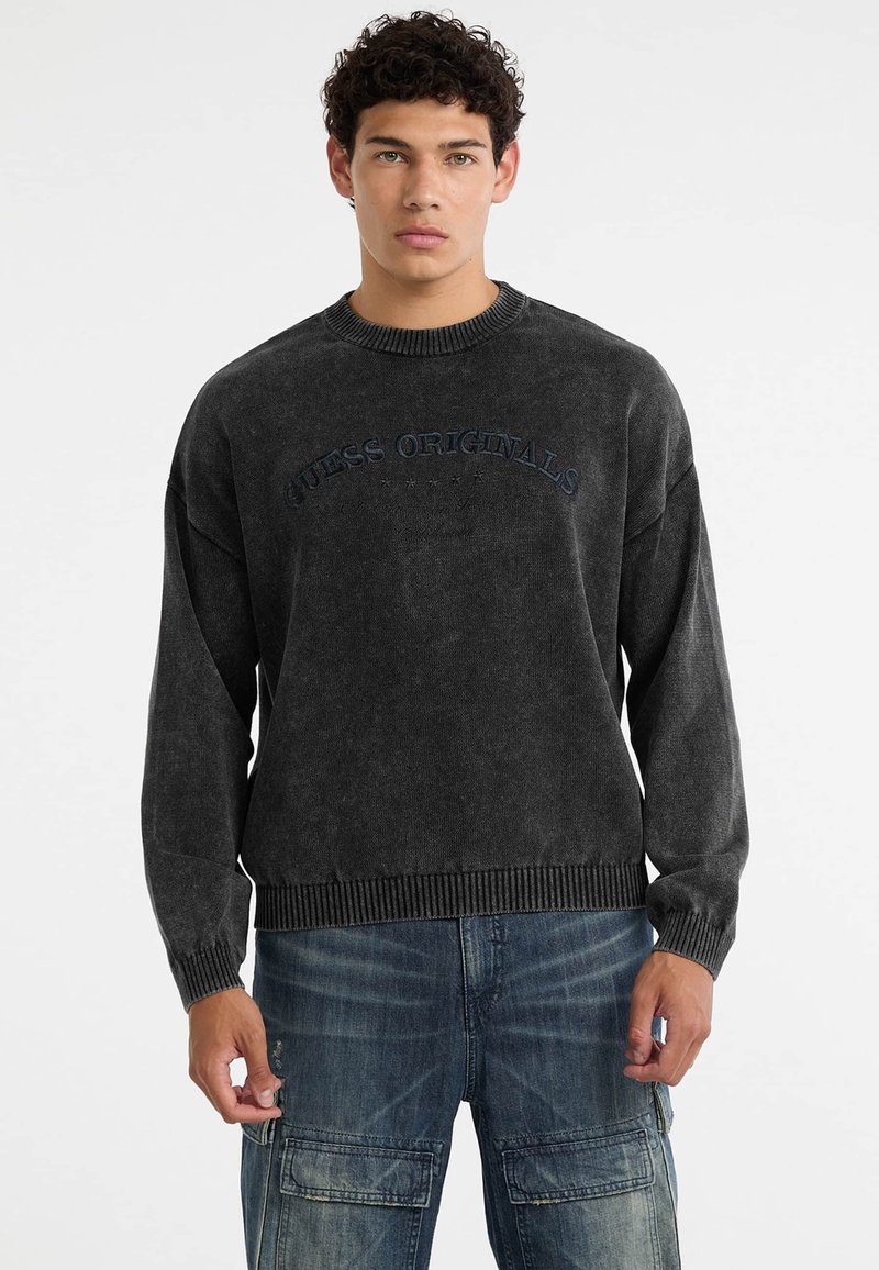 Donkergrijze sweatshirt met ribbels bij de halslijn en mouwen. Bevat het "GUESS ORIGINALS" logo in het blauw, casual oversized ontwerp met een gestructureerd oppervlak.