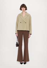 Veste beige à double boutonnage avec des revers surdimensionnés, associée à un pantalon pattes d'eph marron. Des escarpins noirs à bout pointu et un petit sac foncé complètent le look.