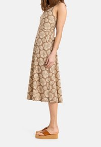 Ruskea kukkakuosiset mekko, jossa on tiukasti istuva yläosa, val流ava A-linjainen hame ja ohuet olkaimet. Yhdistetty ruskeisiin alustakengissä.