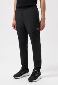 Zwarte stretchbroek met elastische tailleband, zijcargo pockets en meshpanelen. Gecombineerd met zwarte sportschoenen met witte zolen.