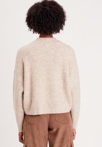 Pull en maille beige clair avec un col rond, coupe ample et ourlet côtelé, affichant une apparence douce et texturée.