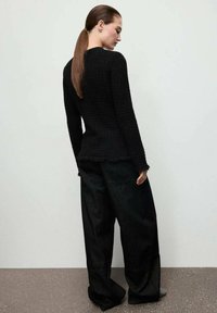 Czarny sweter dziany z postrzępionymi krawędziami, połączony z luźnymi czarnymi spodniami. Materiał wydaje się teksturowany i miękki, tworząc swobodną sylwetkę.