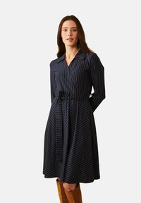 Navy sininen kietaisumekko, jossa on kullanvärisiä pystyraitoja. Mekossa on pitkät hihat, kaulus ja vyötärölle solmittava nauha, ja se on valmistettu sileästä kankaasta.
