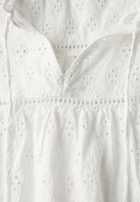 Witte katoenen jurk met bloemembroidery, gehaakte details, een V-hals en een gathered taille. Zachte textuur met een vloeiend ontwerp.