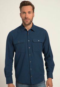 Marineblauw overhemd met lange mouwen en knoopsluiting, voorzien van twee borstzakken, een kraag en knoopsluitingen. Gladde textuur en getailleerde pasvorm.
