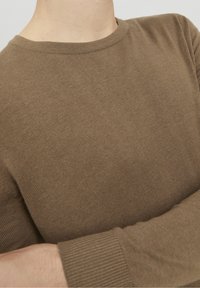 Maglione a maglia marrone con collo rotondo, polsini a coste e una texture morbida. Il tessuto appare leggero e leggermente aderente.