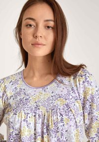Bluse mit Blumenmuster, kurzen Ärmeln in Pastelllila, Gelb und Weiß. Weicher Stoff mit rundem Ausschnitt und dezenten Falten.