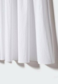 Tissu en coton blanc au toucher lisse, présentant un design plissé avec un drapé doux, créant une apparence fluide et légère.