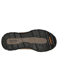 Zwarte rubberen buitenzool met een gestructureerd patroon, voorzien van een centrale bruine zone en "SKECHERS STEADY GRIP" branding. Goodyear-logo aanwezig.