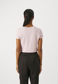 Camiseta corta de color rosa claro con mangas cortas, textura suave y escote redondo, combinada con pantalones negros de corte relajado.