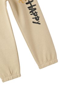 Beżowe dresy bawełniane z elastycznymi mankietami, z czarno-pomarańczowym nadrukiem na lewej nodze. Miękka, teksturowana tkanina dla wygody.