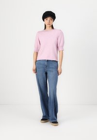 Light pink knit sweater with short puff sleeves, paired with blue flared jeans. The model wears a black beret and dark shoes.