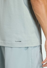 Svetlomodré atletické tričko s jemnou textúrou, krátkymi rukávmi a nápisom "CLIMACOOL" blízko lemu. Nosené s rovnako farebnými šortkami.