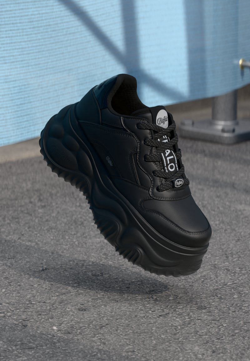 Svart sneaker med en kraftig, skulpturert såle, teksturert svart skinnoppe, snøredesign og fremtredende logo-aksenter på tungen og sidene.