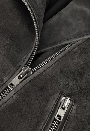 Tessuto di suede nero con texture visibile, dotato di due cerniere argento posizionate in diagonale, che evidenziano un'elegante lavorazione e design.