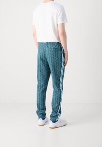 Modré vzorované tepláky s elastickým pasem, bo�čními pruhy a kapsami. Nošené s jednobarevným bílým tričkem a bílou obuví.