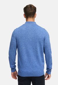 Pull en tricot bleu avec un col rond et des manches longues. Le tissu a une texture douce et un motif uniforme, avec un ourlet côtelé.