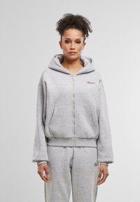 Sivá mikina na zips vyrobená z mäkkej tkaniny s kapucňou, prednými vreckami a ribbovanými manžetami. Obsahuje vyšívaný text na hrudi.